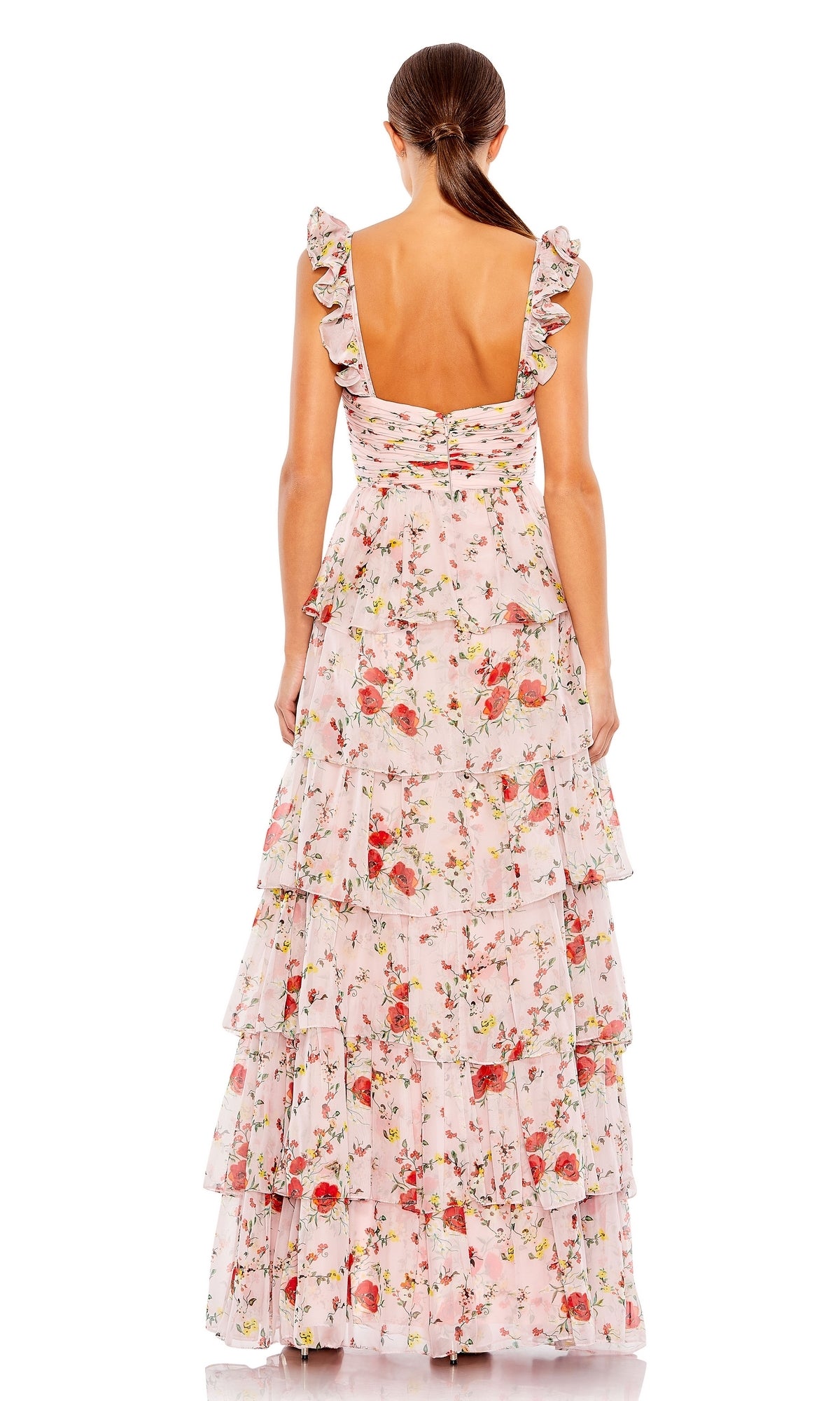 A woman stands facing away in the Long Formal Dress 55816 by Mac Duggal—a sleeveless, pink floral floor-length A-line gown with ruffle layers, low back, and tiered skirt.